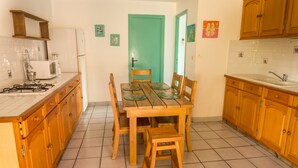 A compact kitchen with wooden cabinets, a tiled floor, a dining table with chairs, and a refrigerator. - Gîte Ixora 4/6 pers in the residence Les Jardins de Pointe Noire, swimming pool (pointe noire)