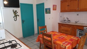 A compact kitchen with teal doors, a dining table with a colorful tablecloth, and a built-in dishwasher. - Gîte Ixora 4/6 pers in the residence Les Jardins de Pointe Noire, swimming pool (pointe noire)
