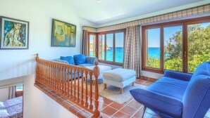 Un vaste espace de vie comprenant un escalier, un canapé, un fauteuil et une vue sur la mer.