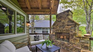 An outdoor deck with a stone fireplace, wicker furniture, and a view of a house. - Mountain Retreat w/ 2 Fireplaces & 3 King Suites (Cashiers)
