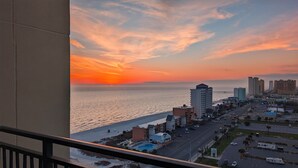 En kystby med solnedgang, der viser et strandhotel, højhuse og en bro i det fjerne.