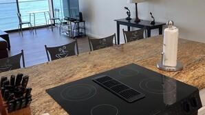 A kitchen with a granite countertop, black stove, and a view of the ocean through large windows. - floor to ceiling windows,180 degree view of ocean, 11th floor (San Diego)