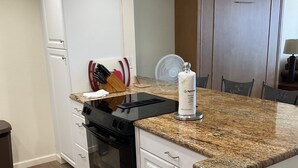 A compact kitchen with white cabinetry, a black stove, and a granite countertop. - floor to ceiling windows,180 degree view of ocean, 11th floor (San Diego)
