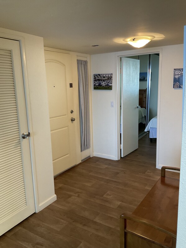 A hallway with wooden flooring, white walls, and a ceiling light fixture. There are doors on the left and a bed visible in the background. - floor to ceiling windows,180 degree view of ocean, 11th floor (San Diego)