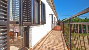 A balcony with a tiled floor, a metal railing, and a white building with windows and shutters.