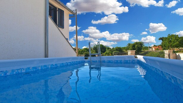 A swimming pool with clear blue water, a ladder, and a view of the sky with clouds.