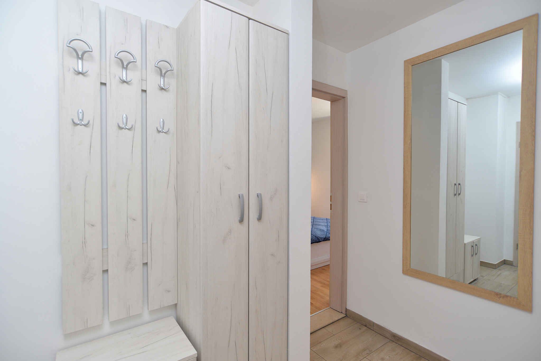 Une pièce dotée d’une armoire avec plusieurs crochets, d’un grand miroir et d’une porte donnant sur une autre pièce.