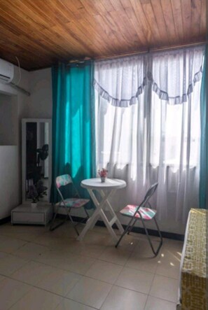 Cozy living space with a dining area, featuring a table and two chairs, a window with sheer curtains, and a comfortable atmosphere.