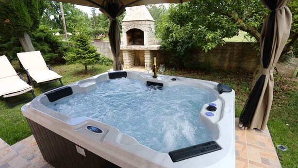 A hot tub with jets, surrounded by a patio area with lounge chairs and a stone oven structure in the background. - Holiday apartment with terrace and whirlpool in the garden (Maružini)