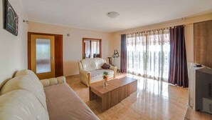 A living room with a sofa, a coffee table, a television, and a window with curtains. - Holiday apartment with terrace and whirlpool in the garden (Maružini)