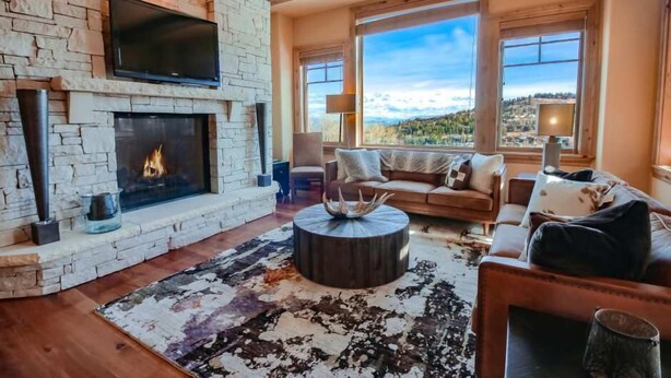 A cozy living room with a stone fireplace, a flat-screen TV, and a large window offering a scenic view. - Silver Strike by Park City Vacations (Park City)