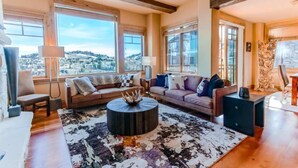 A spacious living room with large windows offering a view of a snowy landscape, a round coffee table, and a sofa with multiple cushions. - Silver Strike by Park City Vacations (Park City)
