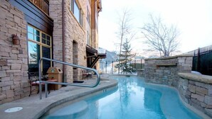 A pool area with a stone wall, a metal handrail, and a wooden deck with chairs. - Silver Strike by Park City Vacations (Park City)
