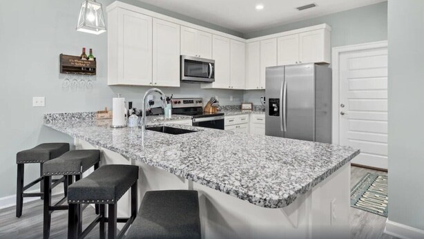 A modern kitchen with white cabinets, a granite countertop, stainless steel appliances, and bar stools. - Comforts of home and just a 5 min walk to the beach! Plus private pool (Panama City Beach)