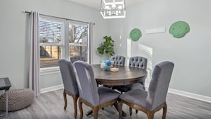 A dining room with a round table, six grey upholstered chairs, a hanging light fixture, a potted plant, and a window with blinds. - Comforts of home and just a 5 min walk to the beach! Plus private pool (Panama City Beach)