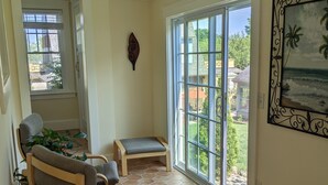 A sunlit room with a large sliding glass door leading to a backyard, a wooden bench, and a cushioned chair.