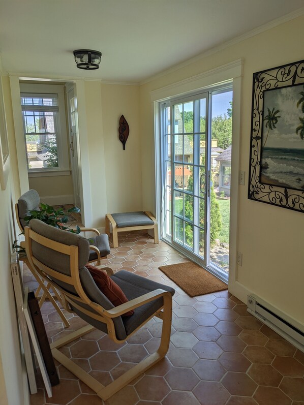 A sunlit room with a large sliding glass door leading to a backyard, a wooden bench, and a cushioned chair.
