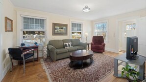 A living room with a sofa, armchair, coffee table, TV, and a desk.