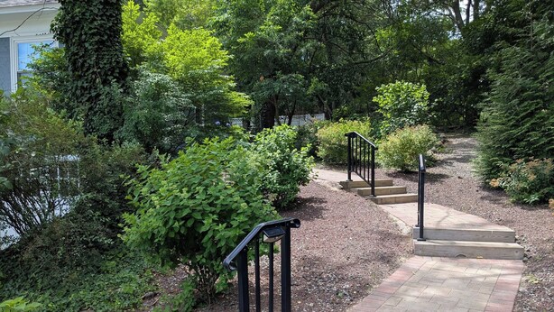 A garden pathway with steps leading to a house, surrounded by lush greenery and trees.