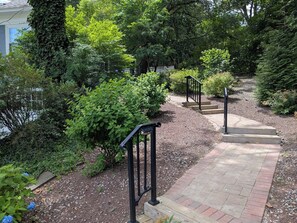 A garden pathway with steps leading to a house, surrounded by lush greenery and trees.