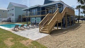 A modern two-story building with a pool, outdoor seating, and a wooden staircase. - Seabatical - Oceanfront in Garden City Beach, SC (Garden City Beach)