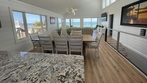 A spacious kitchen with a granite countertop, a dining area with white chairs, and a large window overlooking the ocean. - Seabatical - Oceanfront in Garden City Beach, SC (Garden City Beach)