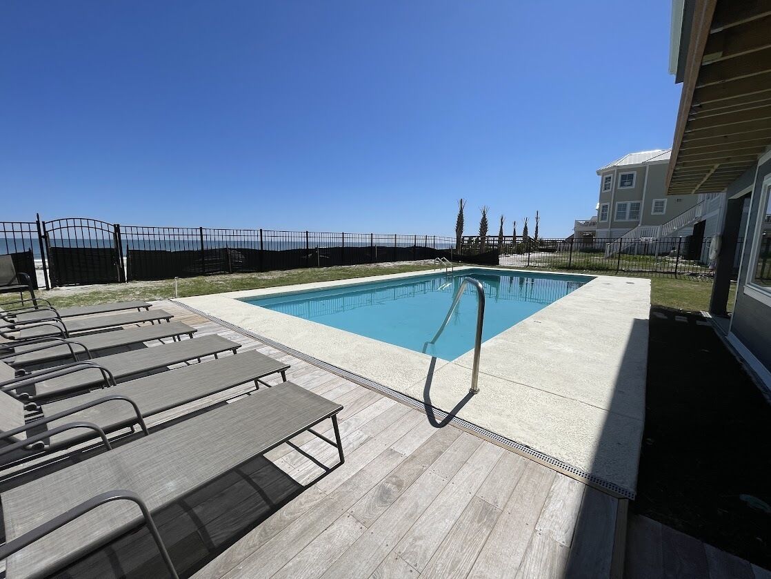 En swimmingpool med solstolar och ett staket, omgiven av en byggnad med ett platt tak.