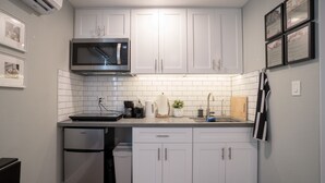 Une cuisine compacte avec des meubles blancs, un four à micro-ondes encastré, une machine à café et un petit réfrigérateur.