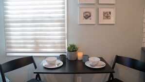 Un coin repas avec une table dressée pour deux personnes, une plante en pot et des tableaux encadrés accrochés au mur.
