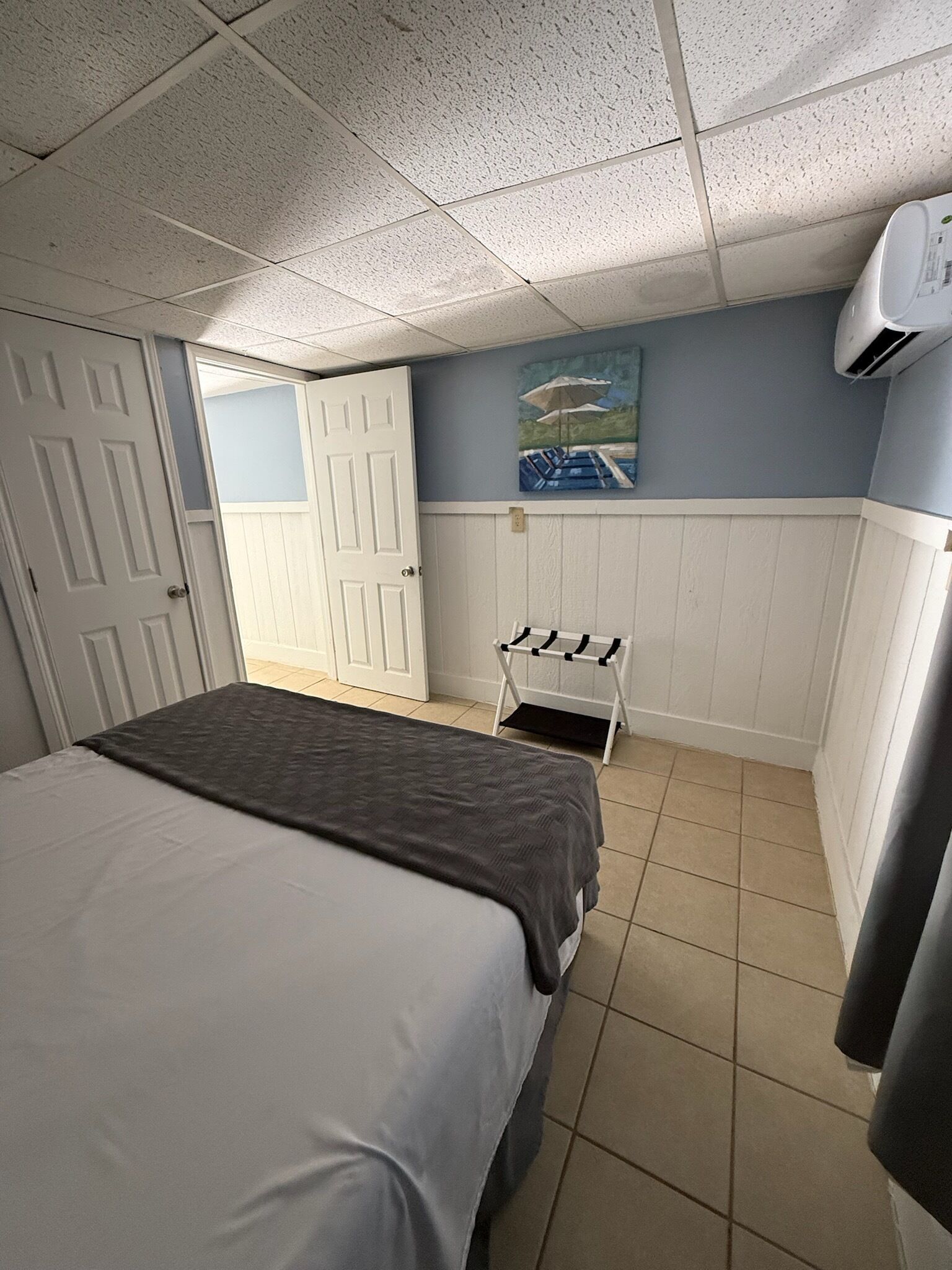 Una habitación de hotel con cama, un cuadro en la pared, una puerta y un equipo de aire acondicionado.