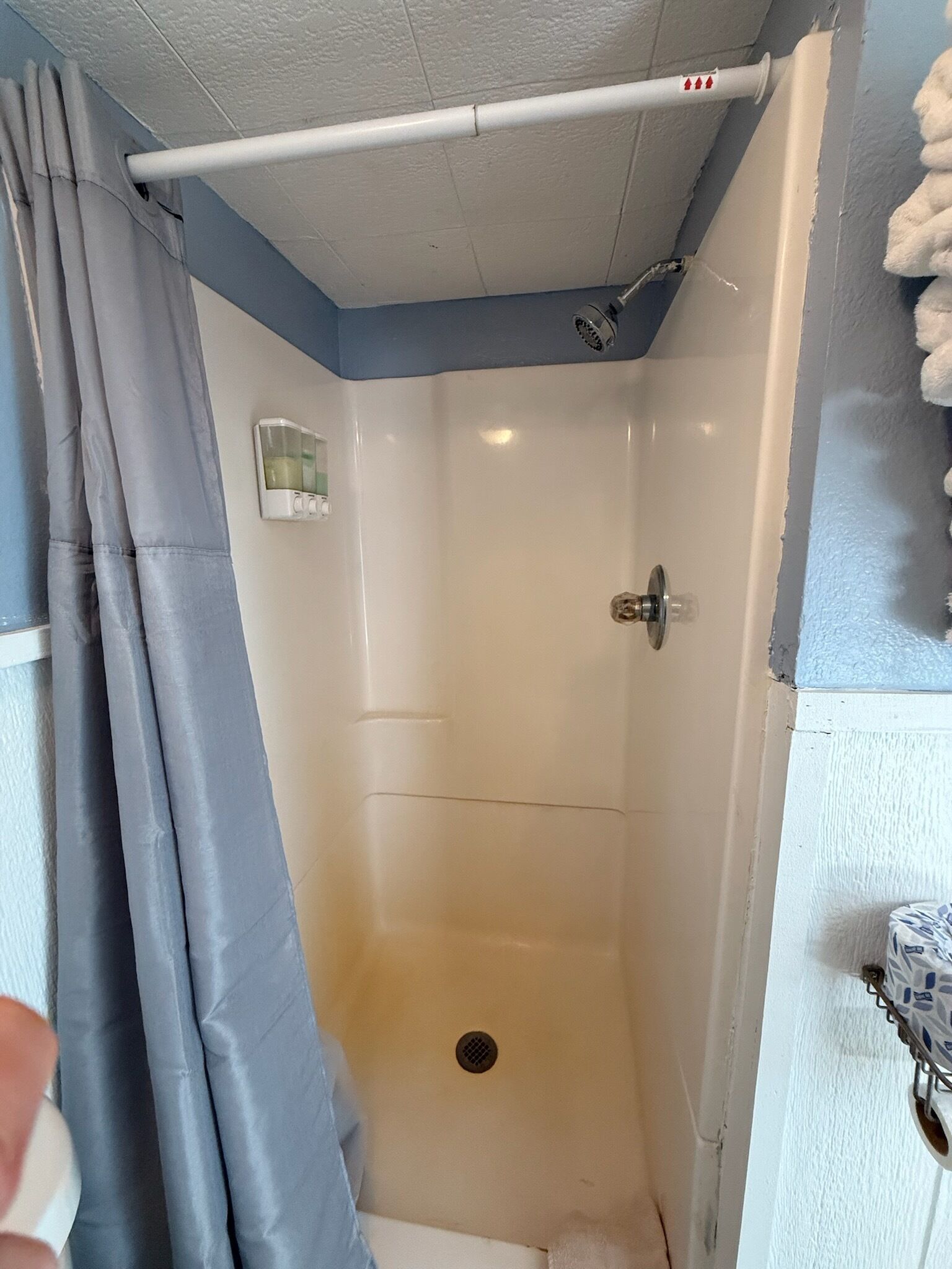 Un espacio de ducha pequeño y cerrado, con rociador, desagüe y toallero en la pared.