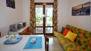Un salón acogedor con un sofá de colores, una mesa de comedor con juego de té, un televisor y vistas al exterior a través de una puerta de cristal.