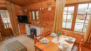 Accogliente interno di una baita in legno con un tavolo da pranzo per quattro persone, un caminetto, pareti in legno e ampie finestre che offrono vista all'esterno.