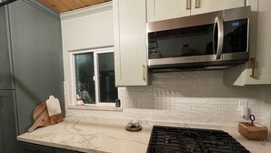 A kitchen with white cabinets, a stainless steel microwave, a gas stove, and a window with a view of the outside.