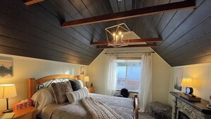 A cozy bedroom with a wooden bed, a fireplace, and a window with curtains.