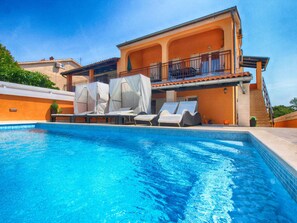 A swimming pool with lounge chairs and umbrellas, a covered outdoor seating area, and a two-story building with a balcony.