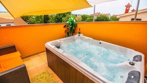 Un jacuzzi en un balcón con una sombrilla amarilla, una silla de mimbre y un tapete estampado.