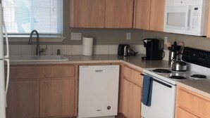A compact kitchen with wooden cabinets, a white dishwasher, a microwave, a stove, and a sink. - Private, comfy and cozy apartment in family neighborhood (Oregon City)