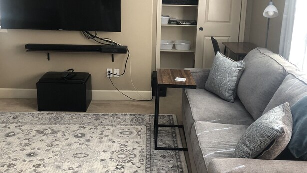 A living room with a flat-screen TV, a sofa, a coffee table, a rug, and a storage unit with shelves. - Private, comfy and cozy apartment in family neighborhood (Oregon City)