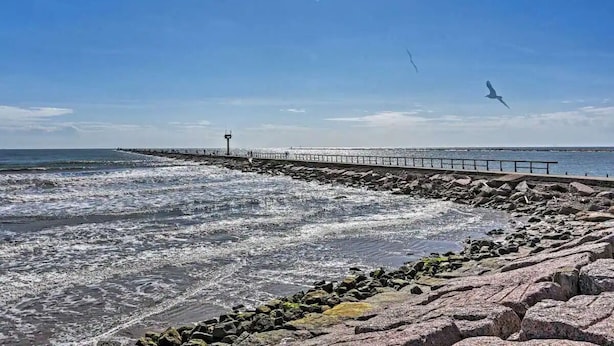 Una costa rocosa con olas rompiendo en la playa y un muelle que se adentra en el agua.
