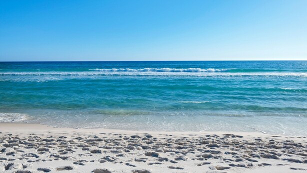 Une plage avec une eau d’un bleu limpide et un rivage sablonneux.