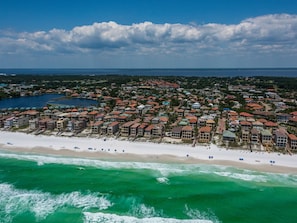 Vista aérea de uma área residencial costeira com propriedades à beira-mar, um porto de iates e uma praia com guarda-sóis.