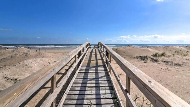 A wooden boardwalk leading to a beach with dunes and the ocean in the background.