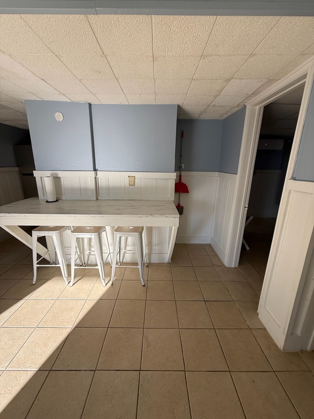A kitchen with a white table and stools, a red broom, and a white door.