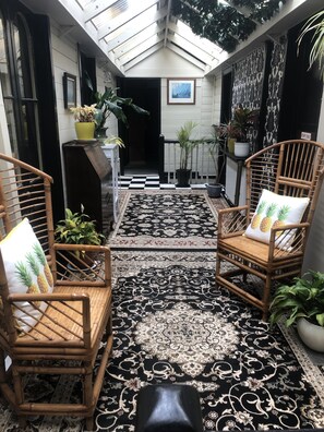 Relax in a serene outdoor seating area with two wicker chairs and potted plants, surrounded by a glass ceiling.