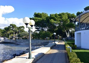 A waterfront promenade with stone steps, lamp posts, and a white building with a covered area.