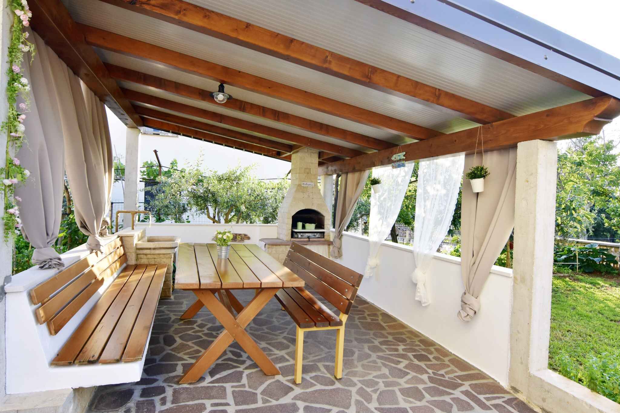 An outdoor patio with a wooden table and benches, a stone floor, and a brick fireplace.
