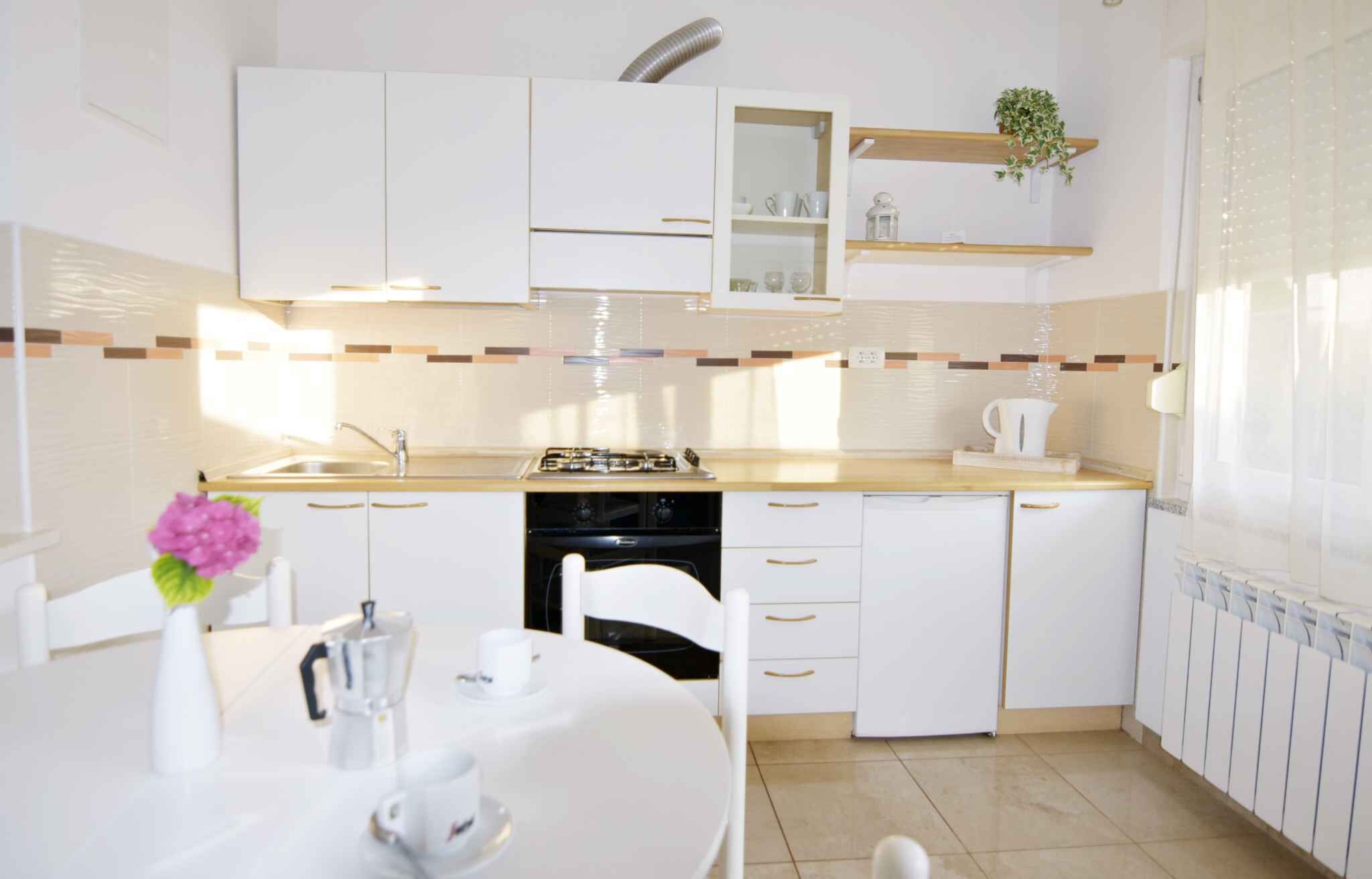 Une cuisine moderne avec des meubles blancs, un plan de travail, un évier et une cuisinière. On y trouve une table à manger avec des chaises et un vase rempli de fleurs.