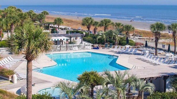 Un resort con piscina, vistas a la playa y palmeras.