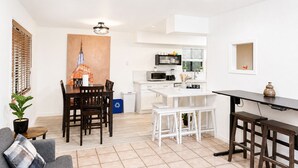 A modern kitchen with white cabinetry, a dining area with a wooden table and chairs, and a small seating area with a sofa and a coffee table. - Midcentury Ranch w/AC, Fully Fenced Yard, 2 Car Garage, WD, 5 HD TVs, Fast WiFi (Flagstaff)